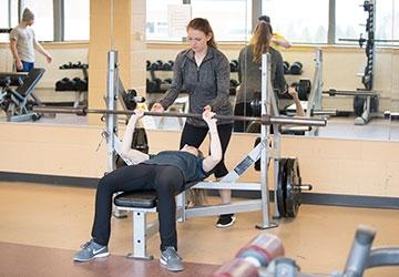 Woman in gym spots person doing a bench press