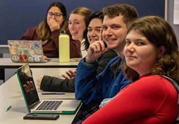 Smiling, engaged students in class at tables with laptops