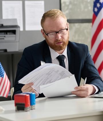 Person at desk looking through papers with american flags in background