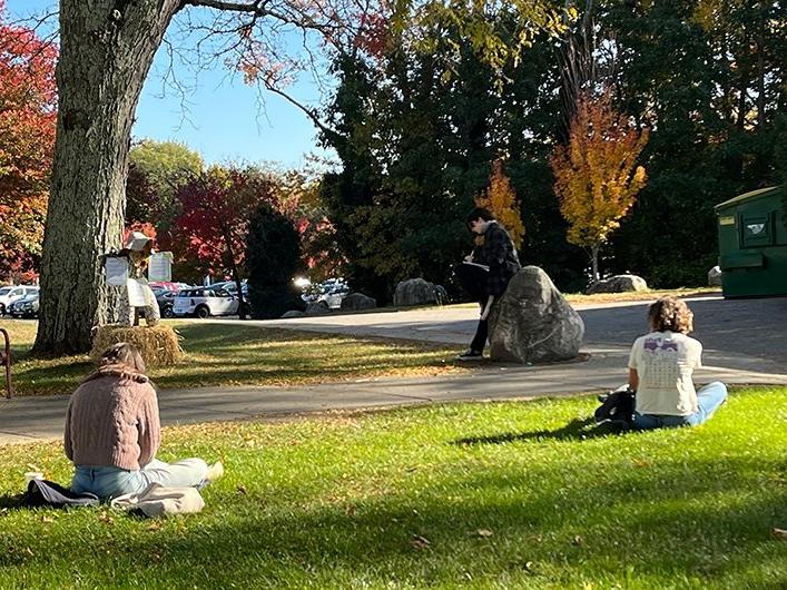 Backs of two people sitting on campus grass, writing in the sunlight