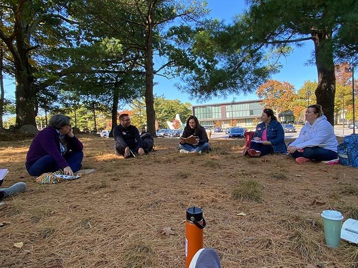 People sitting under trees on campus, sharing their writing