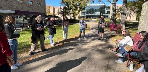 People on campus, standing in a circle, with writing supplies