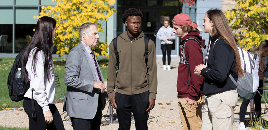 President Warner talking to a small group of students outside, on campus